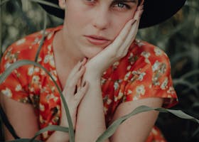 Artistic close-up portrait of a woman in a floral dress and hat outdoors.